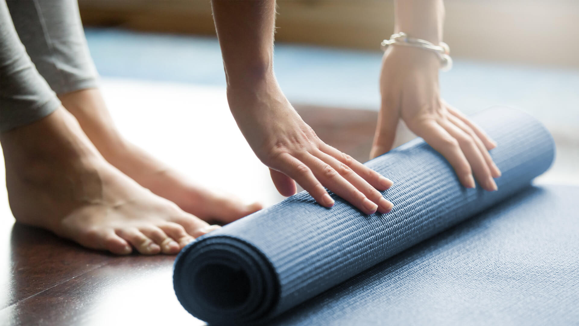Village Physio & Sports Injury Clinic. Physio in Adelaide image of a woman rolling out her yoga mat while standing.