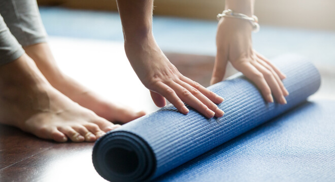 Village Physio & Sports Injury Clinic. Physio in Adelaide image of a woman rolling out her yoga mat while standing.