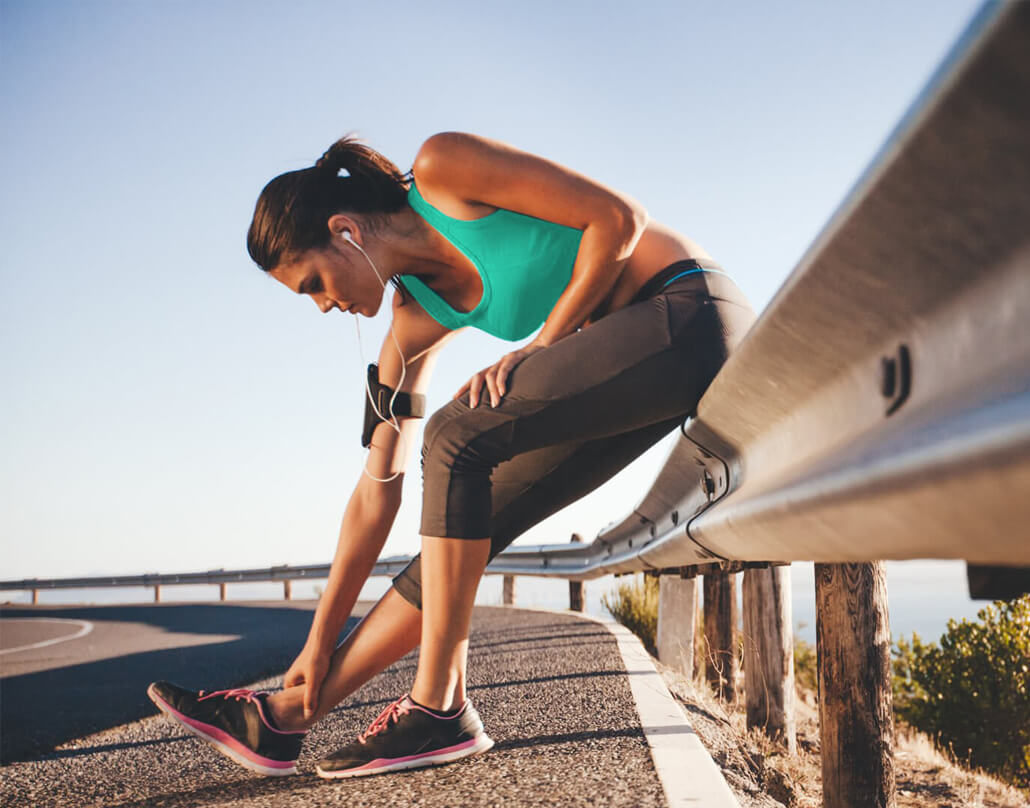 Village Physio & Sports Injury Clinic - Image of a woman doing a leg stretch on the side of the road while out running.